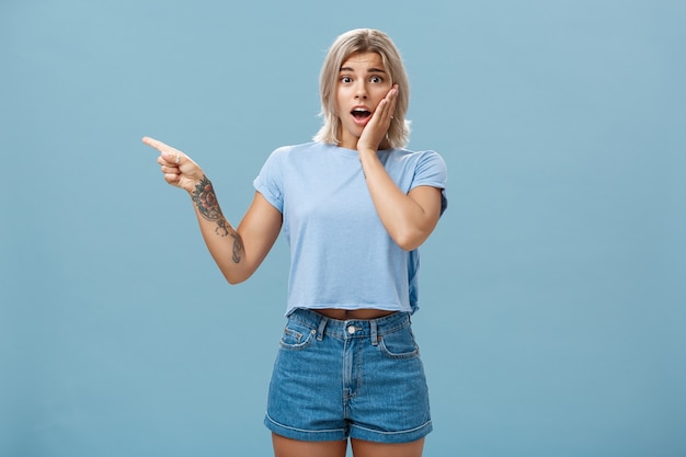 Waist-up shot of worried surprised emotive blonde woman in t-shirt saying gosh opening mouth