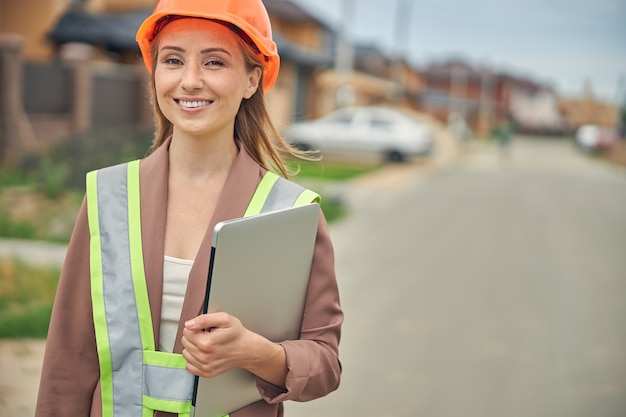 Waist-up a smiling Caucasian female engineer standing in the middle of the street