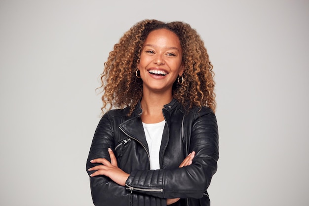 Waist Up Studio Shot Of Happy Young Woman With Folded Arms Wearing Leather Jacket Smiling At Camera