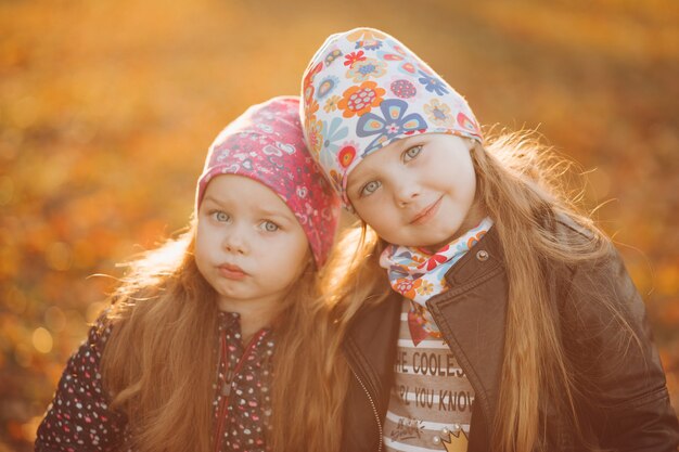 Waist up of two pretty smiling little sisters standing together in the park and hugging. Childhood and happiness concept