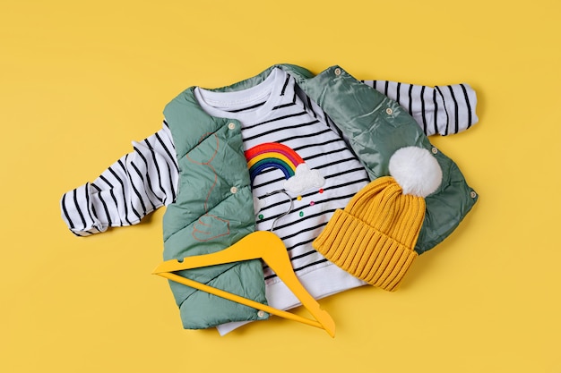 Waistcoat down jacket with striped jumper on yellow background. stylish childrens outerwear. fashion kids outfit