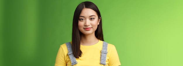 ウエストアップ フレンドリー 陽気な 10 代のアジアの女子大生スタンド 緑の背景 にこやか 素敵な表情 傾向があります。