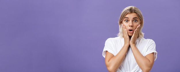 Waistup shot of stunned impressed gorgeous tanned female in white tshirt with blond hair gasping wit