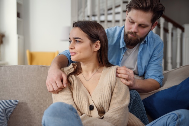 Wait. Worried young man is consoling his girlfriend while touching her arm gently. Woman is holding mobile phone and looking at boyfriend with offence