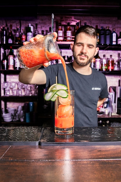 A waiter adds the strained drink to a glass of cocktail on the bar of a bar