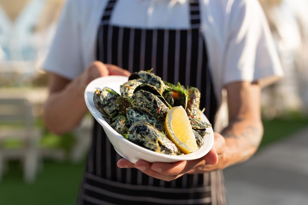 Waiter in an apron offers a tray of mussels and lemon