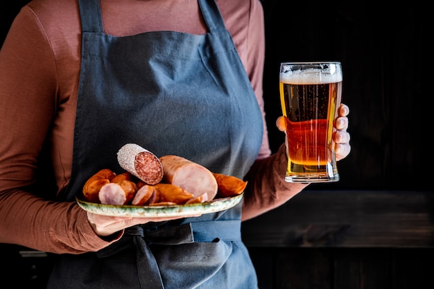 Foto cameriere in aprop detiene bicchiere di birra e salsicce