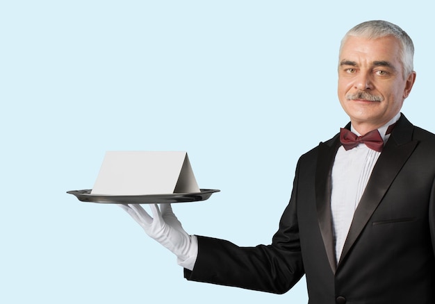 Photo waiter or butler wearing a tuxedo holding a note card on a silver tray in front of his torso