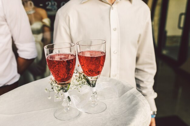 Waiter carries glasses with red drink and decorated with little daisies