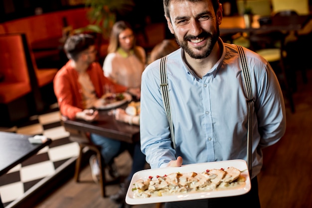 レストランで肉料理とプレートを運ぶウェイター