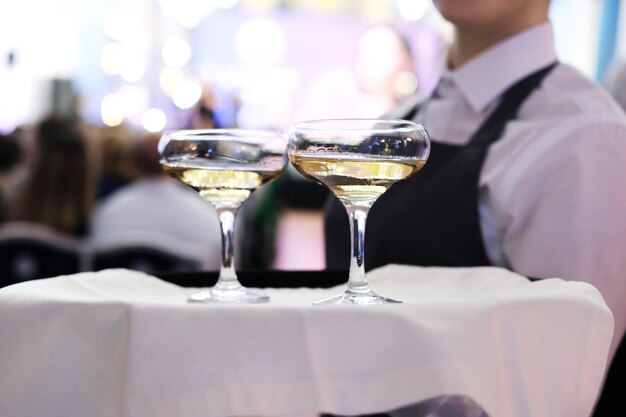 The waiter is holding a tray with two glasses of champagne Catering for the event