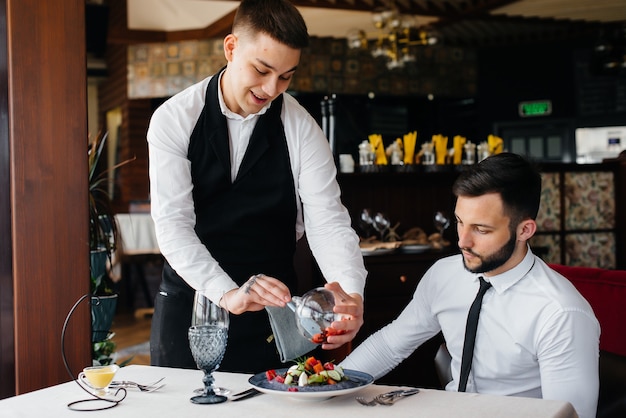 The waiter makes an exquisite serving of seafood salad, tuna and black caviar in a beautiful serving on the table in the restaurant. Exquisite delicacies of haute cuisine close-up.