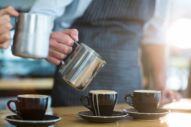 Waiter making cup of coffee at counter in cafe