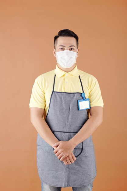 Waiter in medical mask and apron having badge on his chest