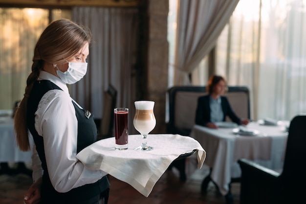 Официант в медицинской маске подает кофе латте