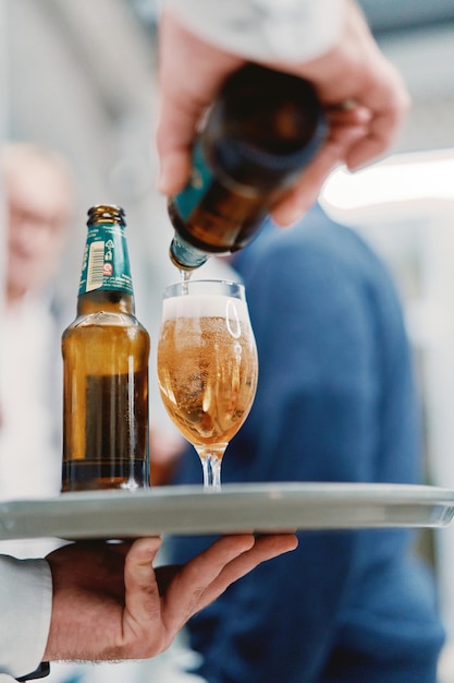 Photo waiter pours beer into a glass on a tray in his hand