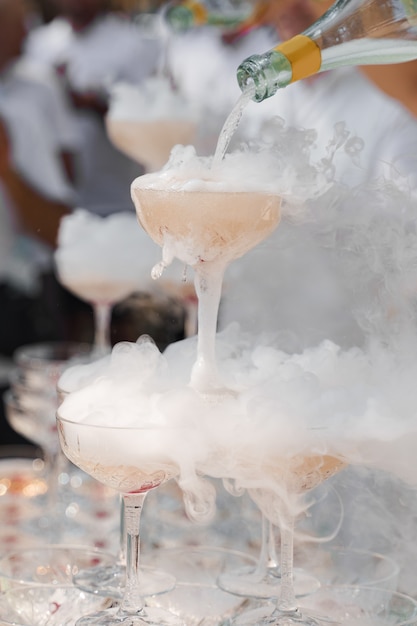 The waiter pours champagne into crystal glasses with dry ice and white smoke close up