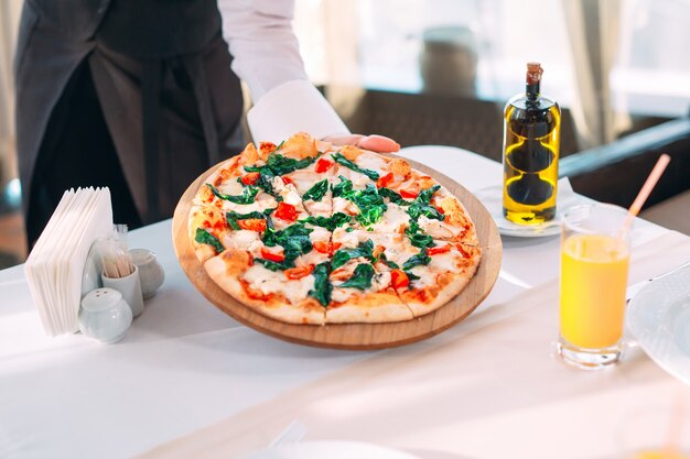 The waiter puts pizza On the table in the Restaurant.