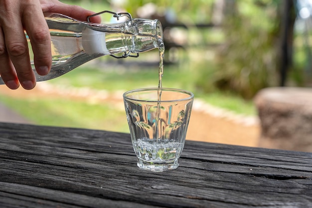 A waiter in a restaurant pours fresh water from a bottle into a glass, close up, outdoors