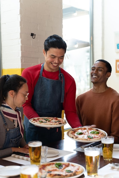 Waiter serves pizza to a group of friends in a cafe drink glasses on the table