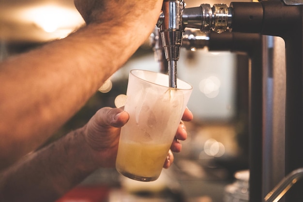 Waiter serving beer in a glass with a beer shooter at a bar.