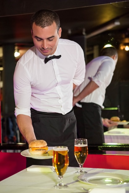 Waiter serving burger and beer on a table in bar