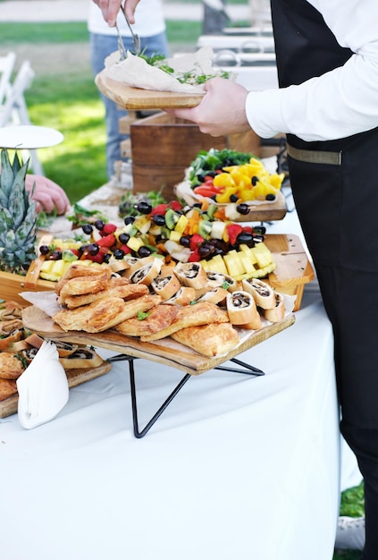 Waiter serving food to guests catering service wedding welcome\
food fruits on skewers and canapes welcome buffet at wedding\
reception