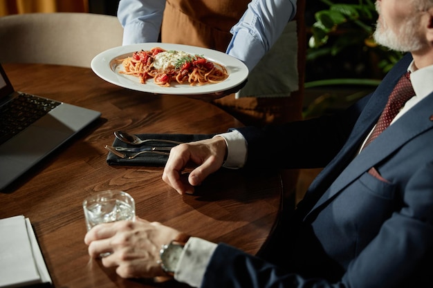 Waiter serving pasta for man in restaurant