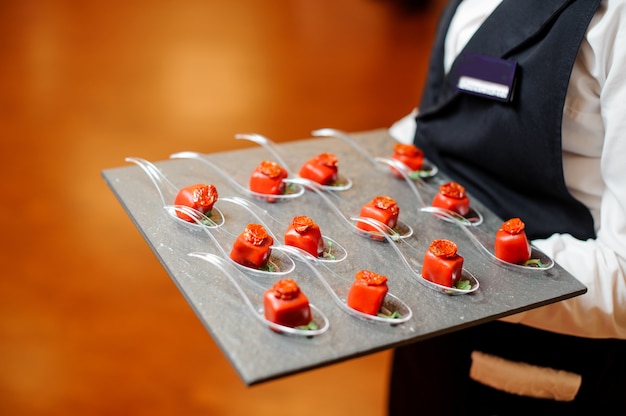 Foto cameriere che serve un patè di piccoli antipasti salati in una glassa rossa decorata con pomodori secchi e microgreens