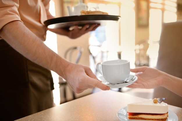 Waiter serving tea to customer in cafe