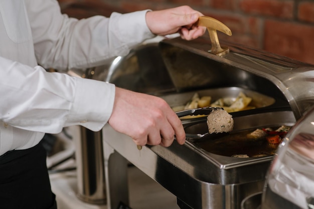 A waiter takes a cuttlet from the bowl on the buffet table