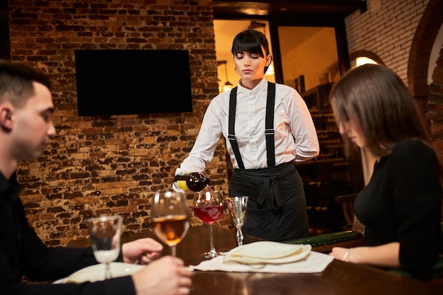 The waiter in uniform pours visitors wine in restaurant