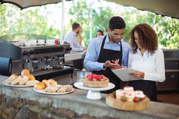 Waiter and waitress discussing on clipboard at counter