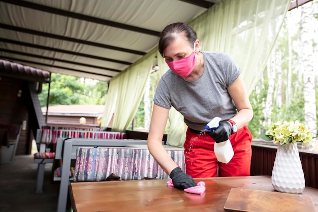 Waiter wearing protective face mask while disinfecting tables at outdoor cafe