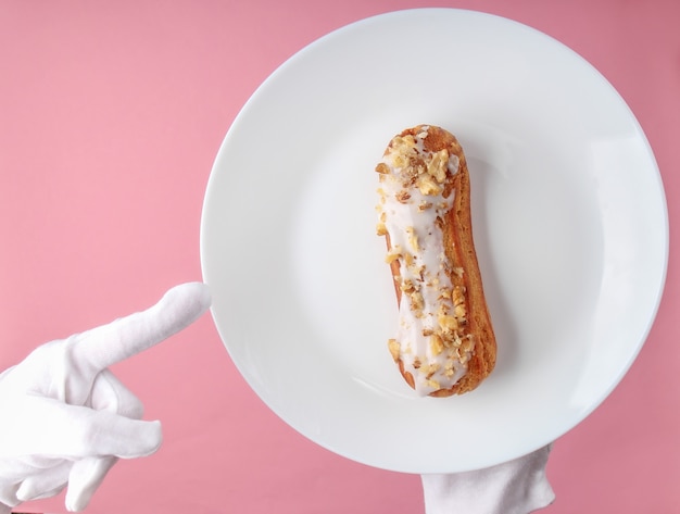 Waiter in white gloves serves eclair on a plate