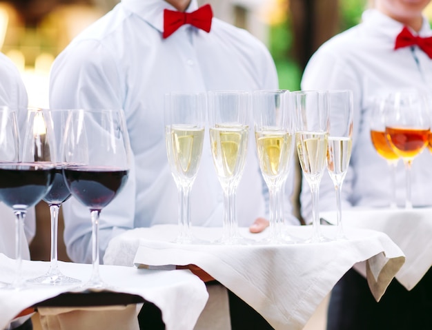 The waiters greet guests with alcoholic drinks. Champagne, red wine, white wine on trays.