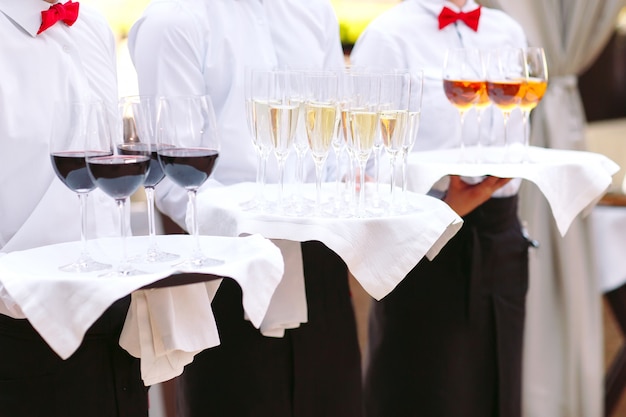 The waiters greet guests with alcoholic drinks. Champagne, red wine, white wine on trays.