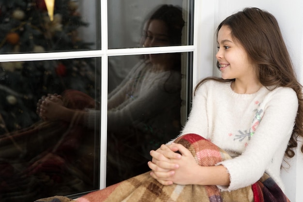 Waiting for Santa Happy winter holidays Small girl at home New year Little girl child looking at window Present xmas Winter memories Kid at home relaxing on cozy window sill Winter feast