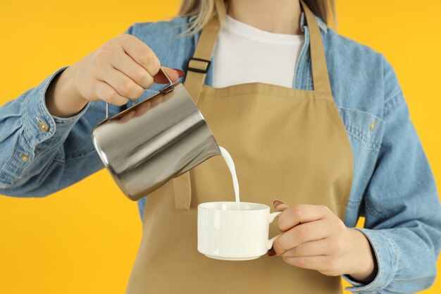 Waitress or barista pour milk on yellow background