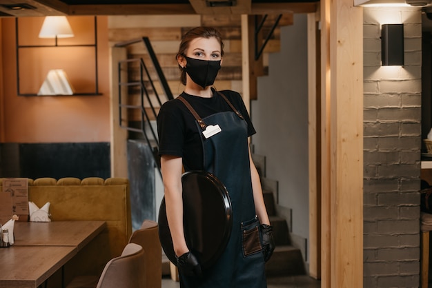 Waitress in black disposable medical gloves wears a medical face mask