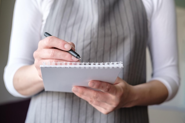 Waitress in a cafe in an apron with a notebook and pen takes an order from the client