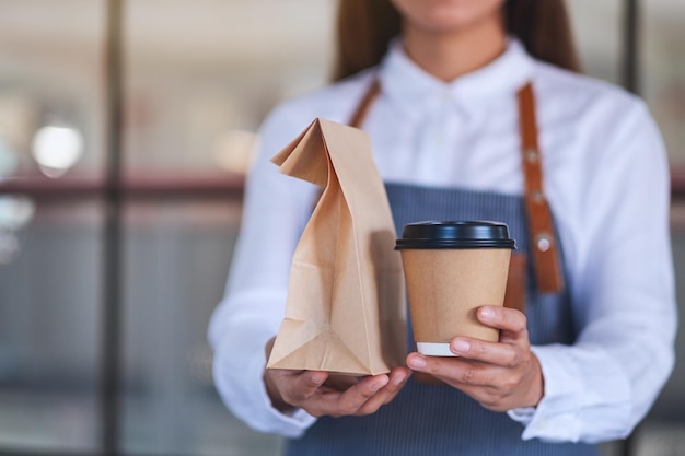 Foto una cameriera che tiene e serve una tazza di caffè di carta e cibo da asporto in un sacchetto di carta al cliente in un negozio