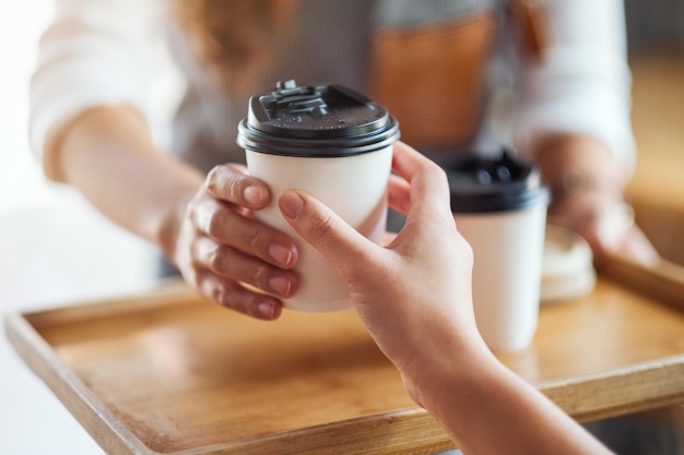 Una cameriera che tiene e serve bicchieri di carta di caffè caldo al cliente al bar