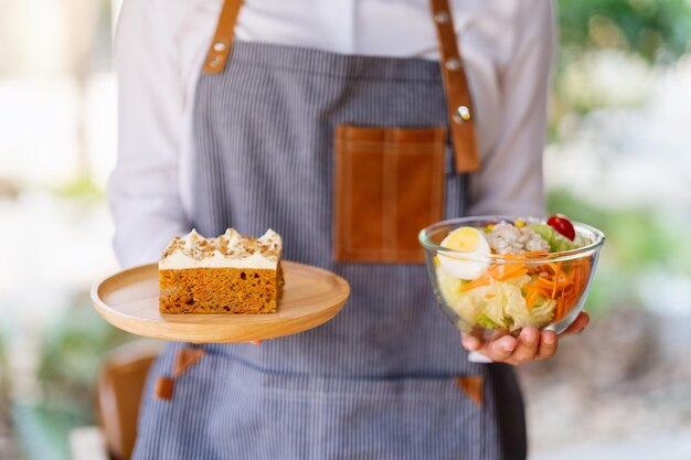 A waitress holding and serving a plate of carrot cake and a bowl of vegetables salad