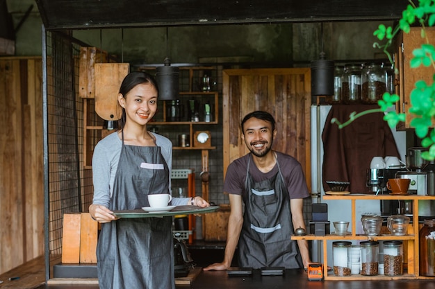 Waitress holding the tray with a cup of coffee on it while the male barista standing inside the bar