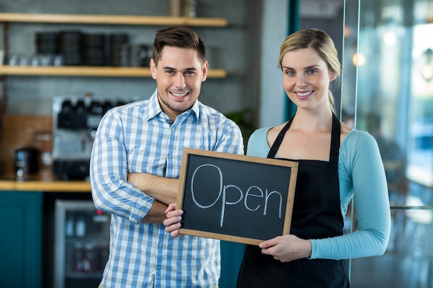 Waitress and man standing with open sign on slate in cafe