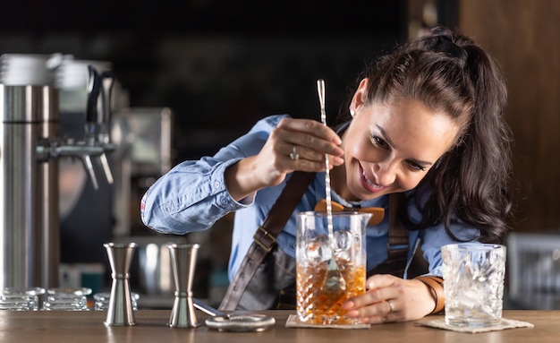 Waitress mixes old fashioned whiskey cocktail in a decorative glass in a pub.