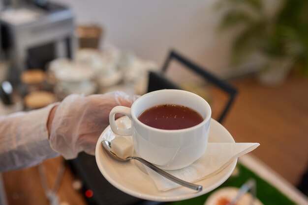 Waitress near table with dishware and different delicious snacks during coffee break closeup