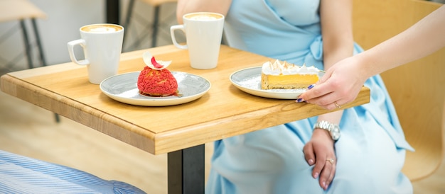 ウェイトレスの手がカフェのテーブルにカップケーキを置き、女性の手が青いドレスを着た女性の背景に小さなペストリーをテーブルに置いています