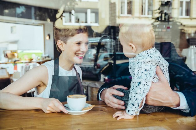 Waitress serving coffee to smiling customer with baby in cafe